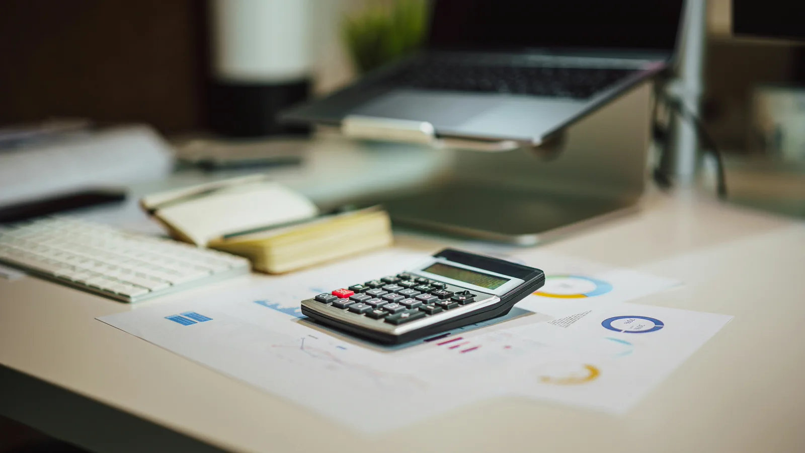 Calculator and laptop on a desk with printed charts