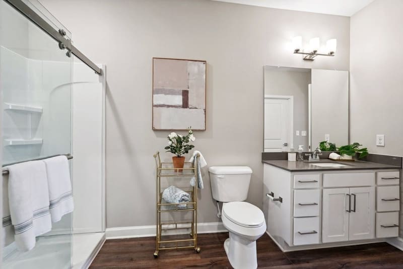 Apartment bathroom vanity with quartz countertop beside a tiled walk-in shower